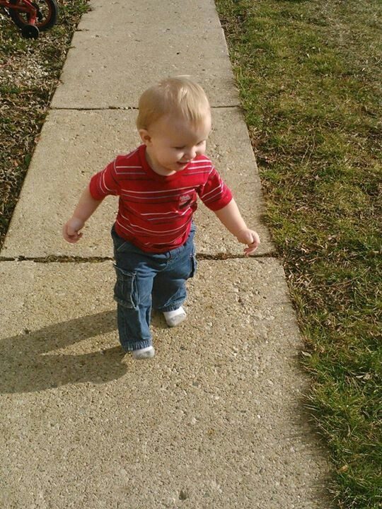 A small child walking along a sunlit pavement.