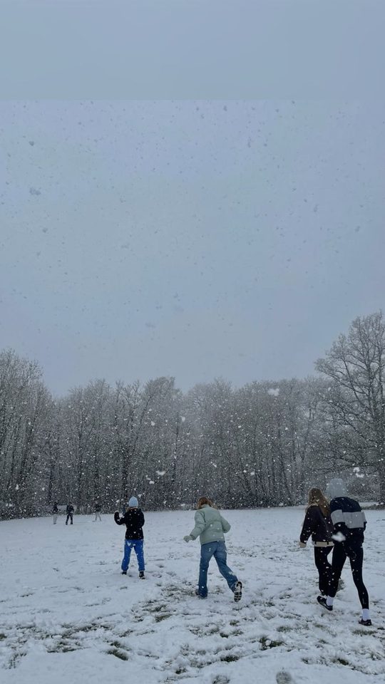 A group of young people running across a snowy field while snow falls.